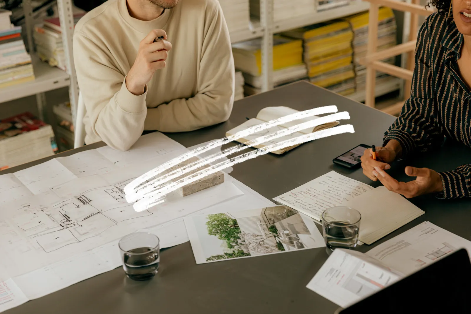 Two people working over drawings and a notebook at a shared desk