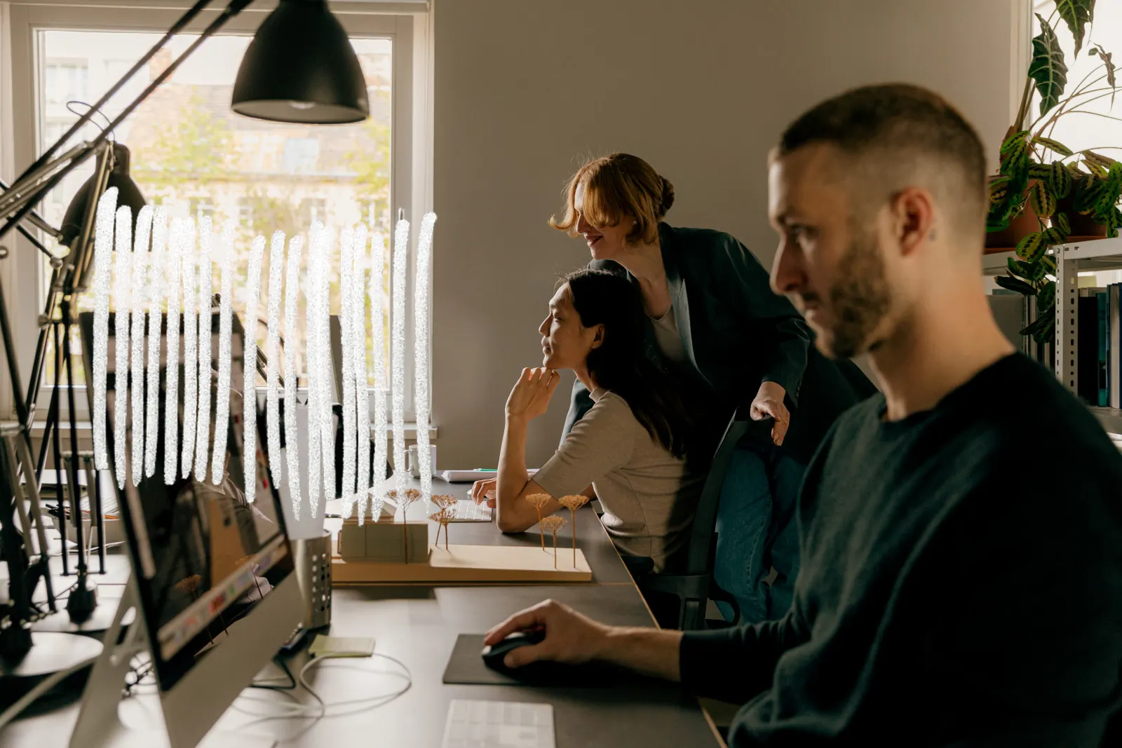 Three people talking around a table of drawings and a model